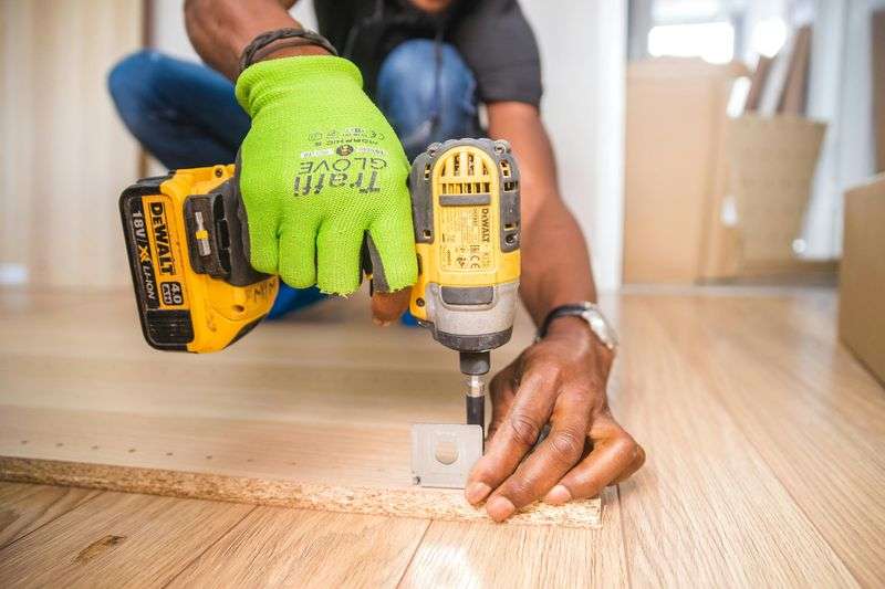 Close-up of a hand using a cordless drill on a wood panel during a construction project