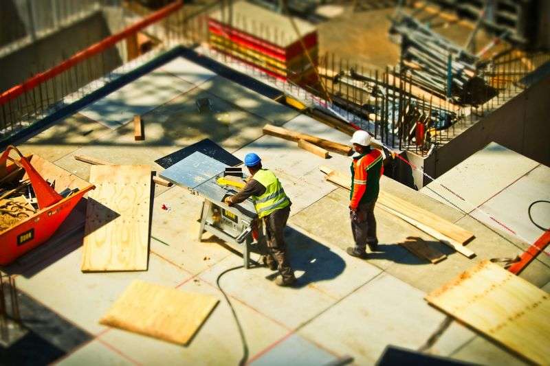 Construction team in hard hats reviewing building blueprints on-site from above