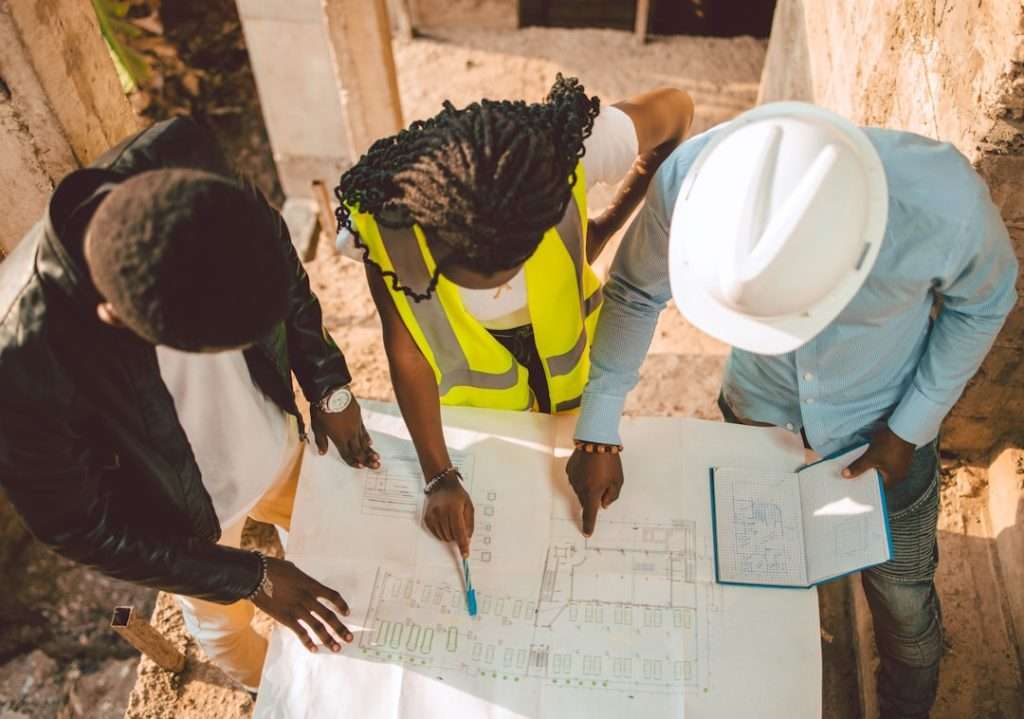 Construction team members in safety gear reviewing blueprints together at a job site