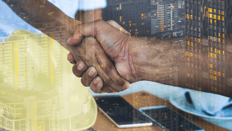 Double-exposed image of a handshake over a city skyline and hard hat, representing a construction business partnership