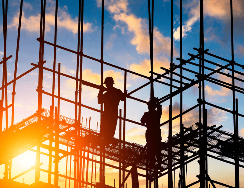 Silhouette of construction workers on scaffolding against a sunset sky